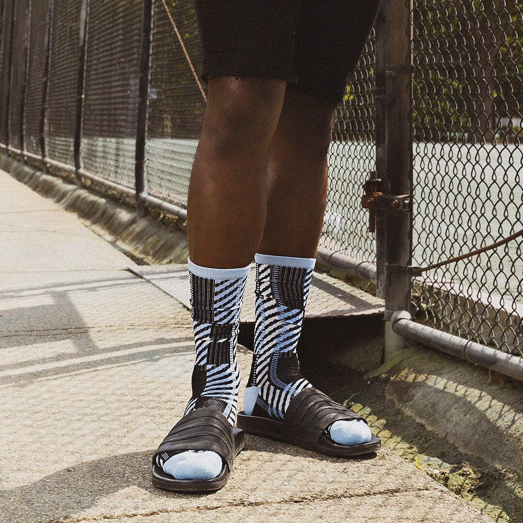 Person wearing black and white striped socks with sandals on a sidewalk.