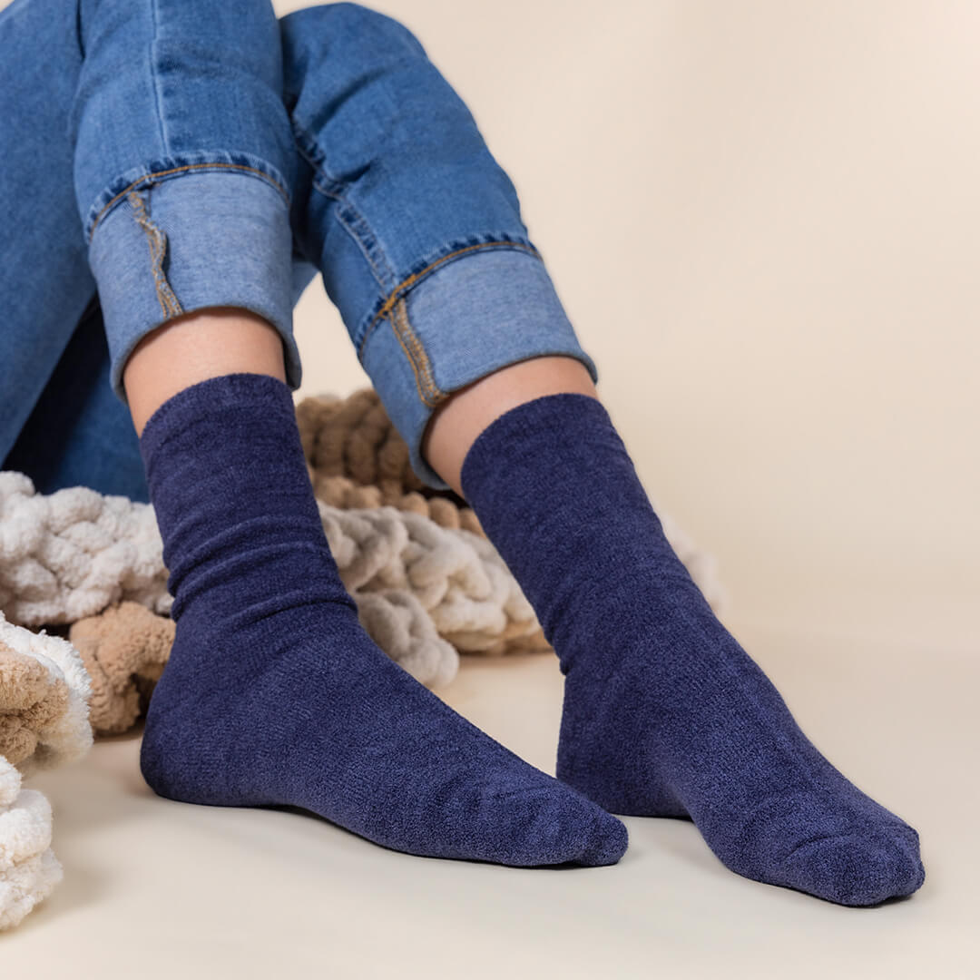 Person wearing blue socks with rolled-up jeans on a neutral background