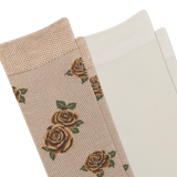 A close-up of a beige sock with a woven rose pattern, brown toe and heel, and another pair of light cream socks.