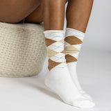 White crew socks with an argyle pattern in brown, beige, and light blue, worn by a model sitting on a woven straw stool. thumbnail