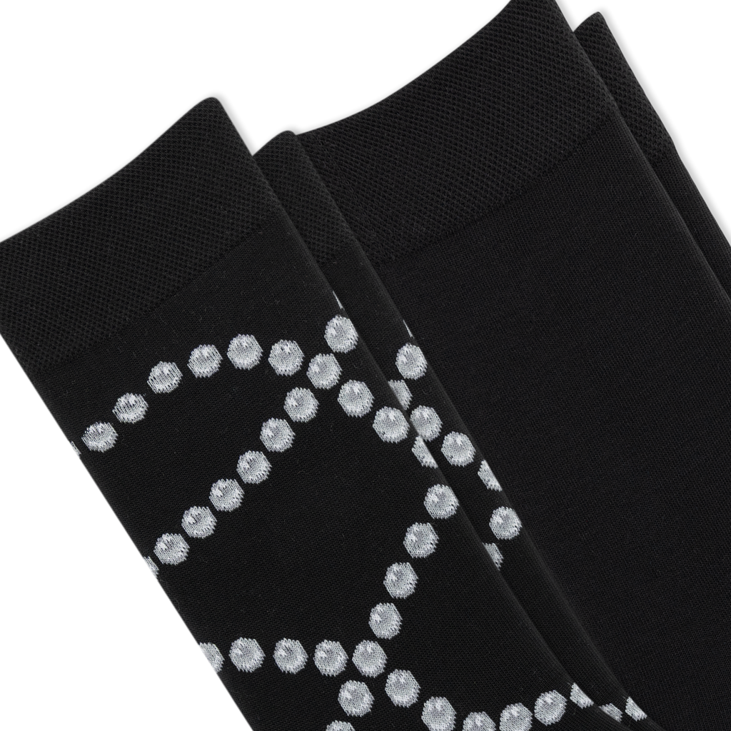Two pairs of black dress socks stacked diagonally, featuring a textured knit pattern with a silver glittery geometric diamond design on the lower half.