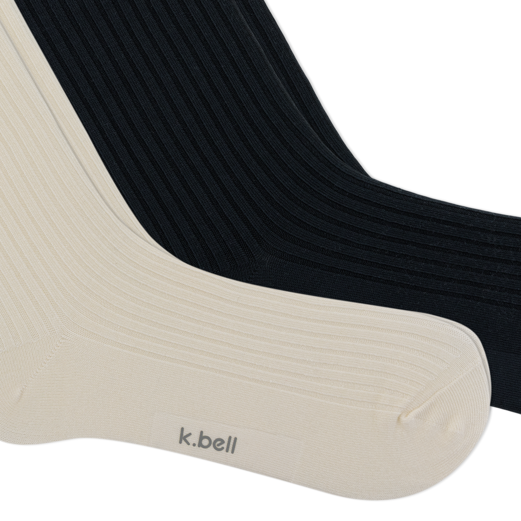 Two ribbed crew socks shown overlapping on a white background, with one sock in warm off-white/cream and the other in black. The cream sock has the brand name 'k.bell' on the foot.