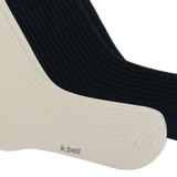 Two ribbed crew socks shown overlapping on a white background, with one sock in warm off-white/cream and the other in black. The cream sock has the brand name 'k.bell' on the foot.