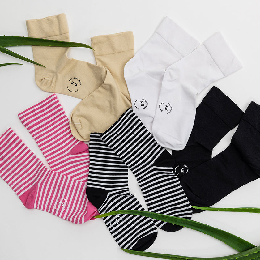 K.Bell striped and solid microfiber crew socks in various colors and patterns on a white background on a light background with green leaves