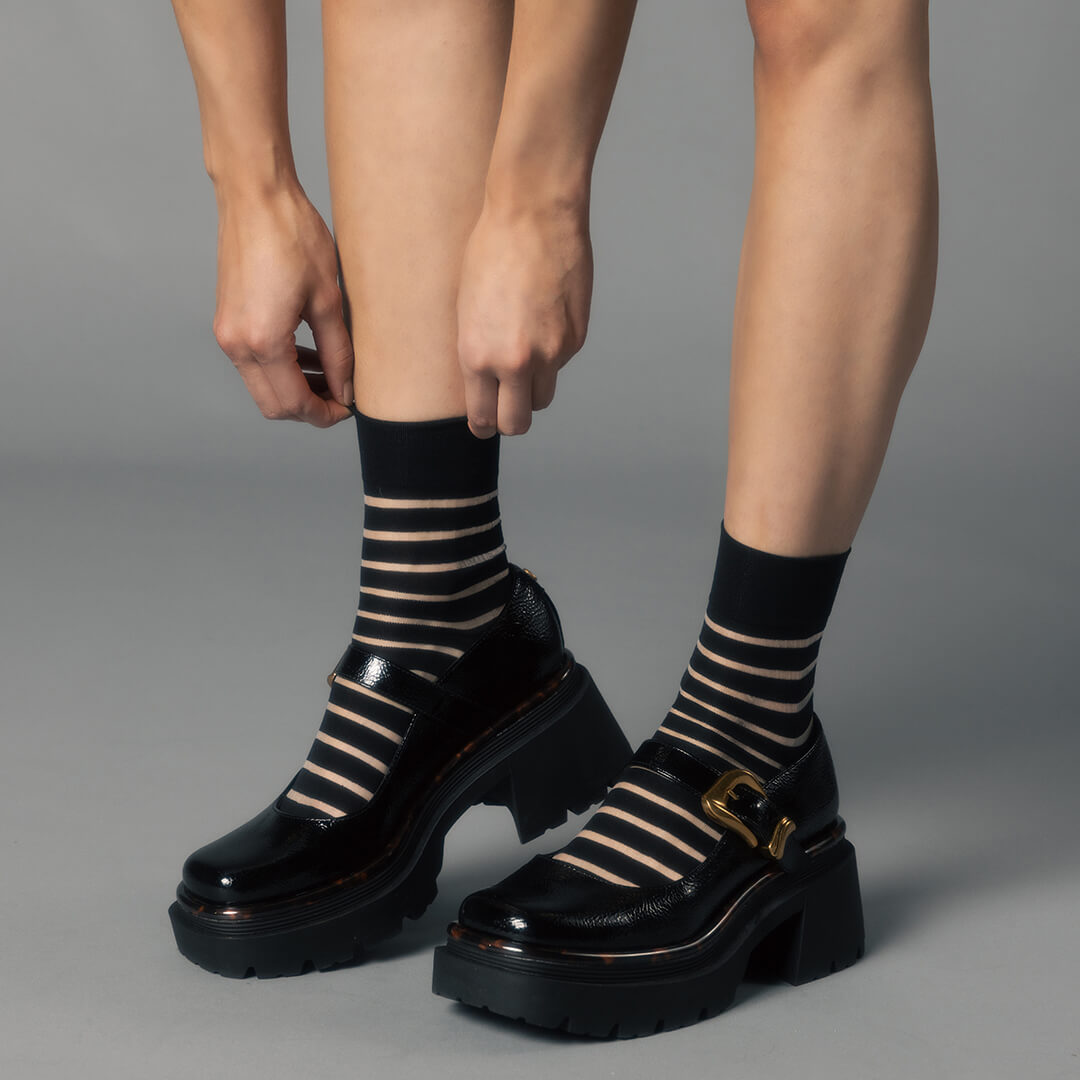 Black platform shoes with striped socks on a gray background