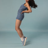 Woman wearing a denim outfit with sneakers and white slouch socks on a light blue background