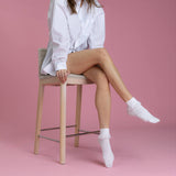 Person sitting on a stool wearing white socks against a pink background