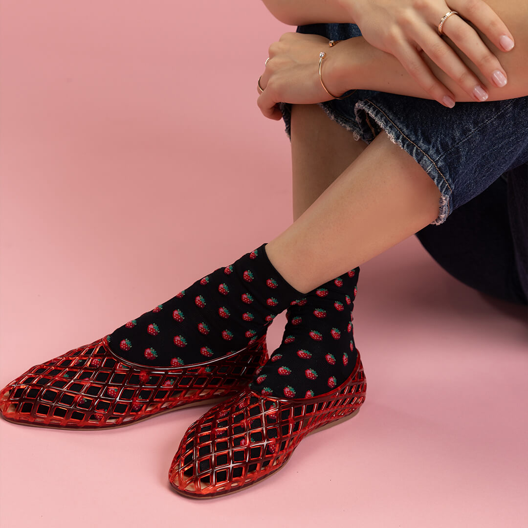 Person wearing red mesh shoes and black socks with red patterns on a pink background