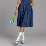 Person wearing a blue denim dress holding blue tulips on a gray background