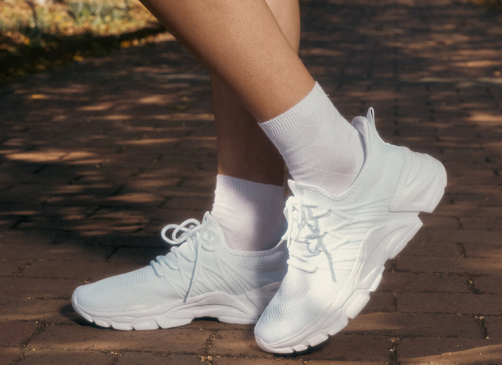 White sneakers worn with white socks on a wooden floor