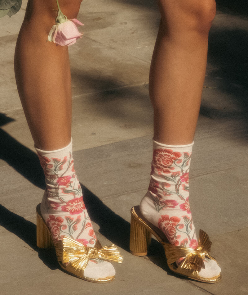 Gold high-heeled shoes with floral patterns worn by a person on a concrete surface.