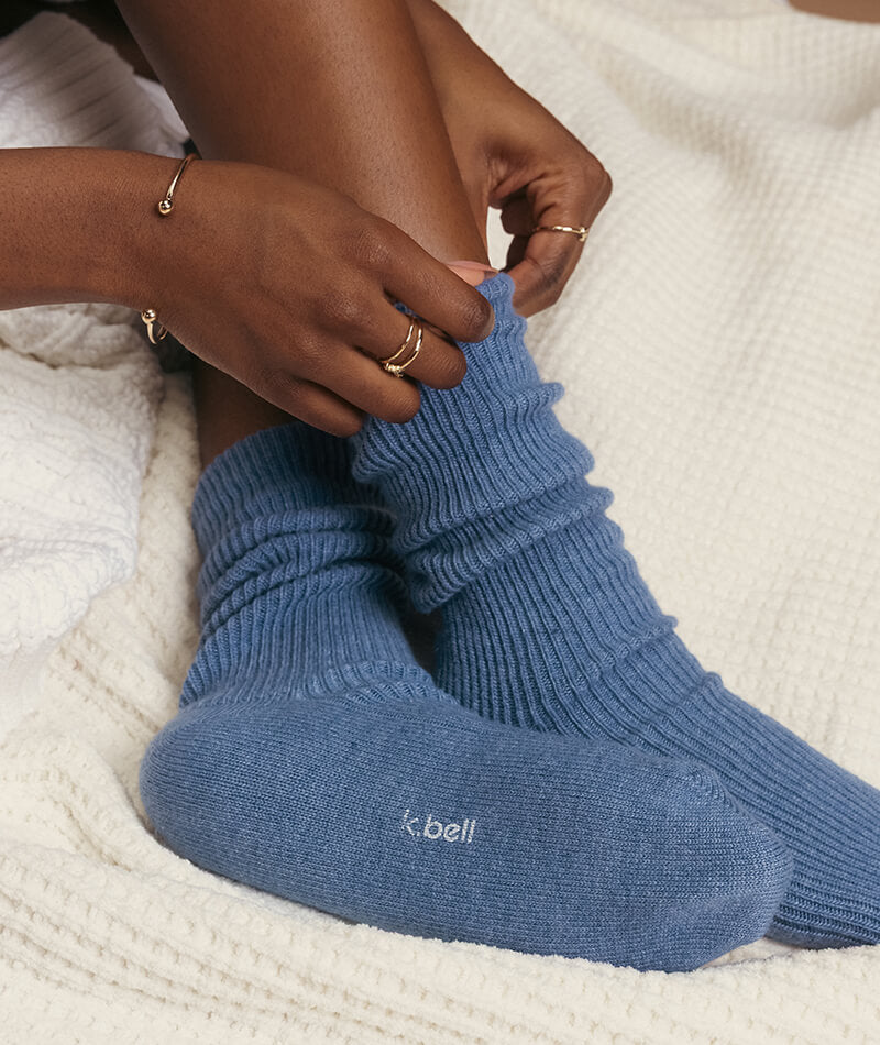 Person wearing blue socks with 'K. Bell' branding on a white textured surface