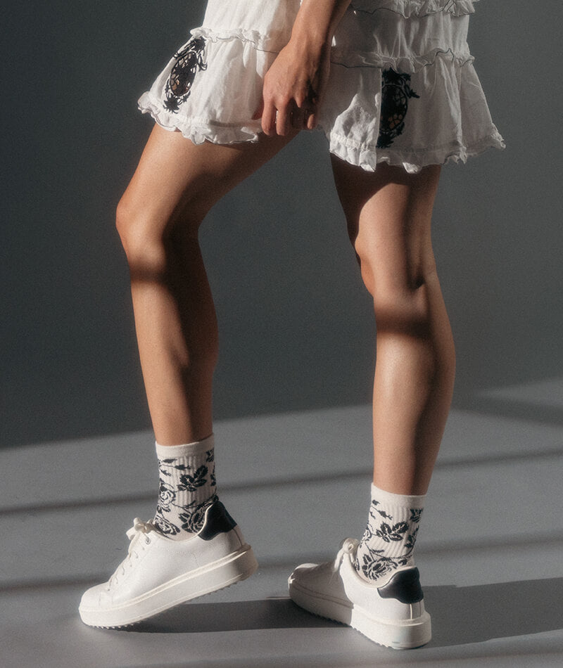 Person wearing white sneakers and patterned socks on a gray background