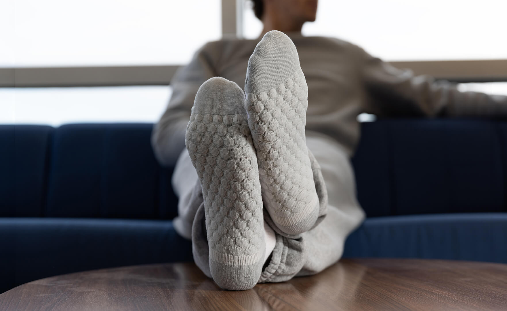 Person wearing light gray textured socks sitting on a couch.
