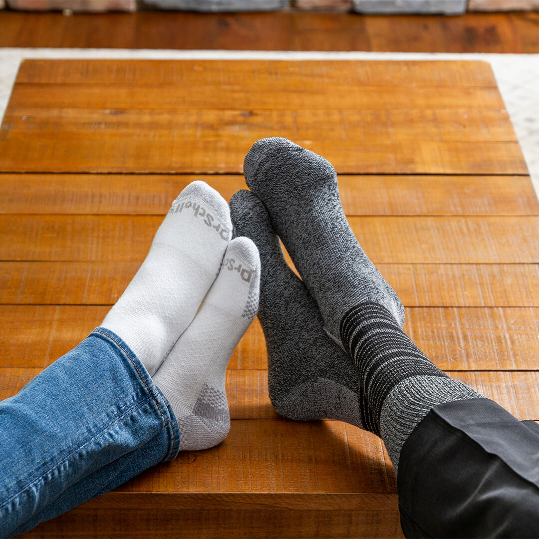 Two pairs of socks, one gray and one white, on a wooden floor.