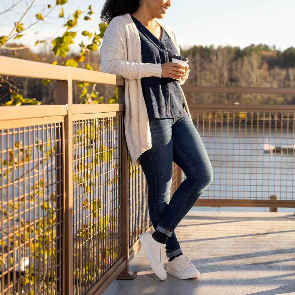 Woman standing on a bridge holding a coffee cup with a scenic background