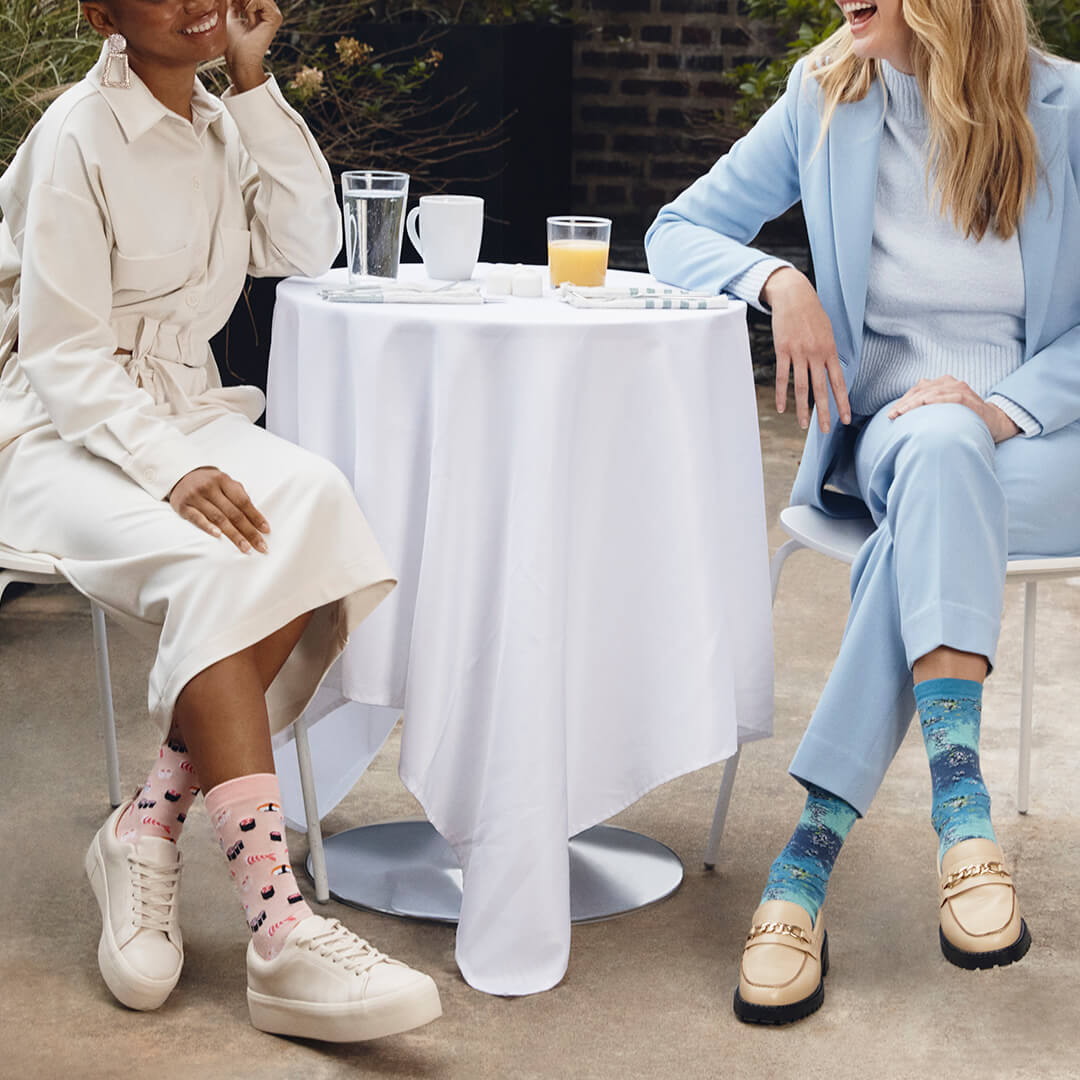 Two women sitting at a table outdoors, wearing colorful socks.