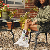Woman sitting on a bench outdoors with plants and a brick wall in the background thumbnail