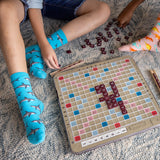 Children playing Scrabble on a carpeted floor with one child wearing shark-patterned socks.