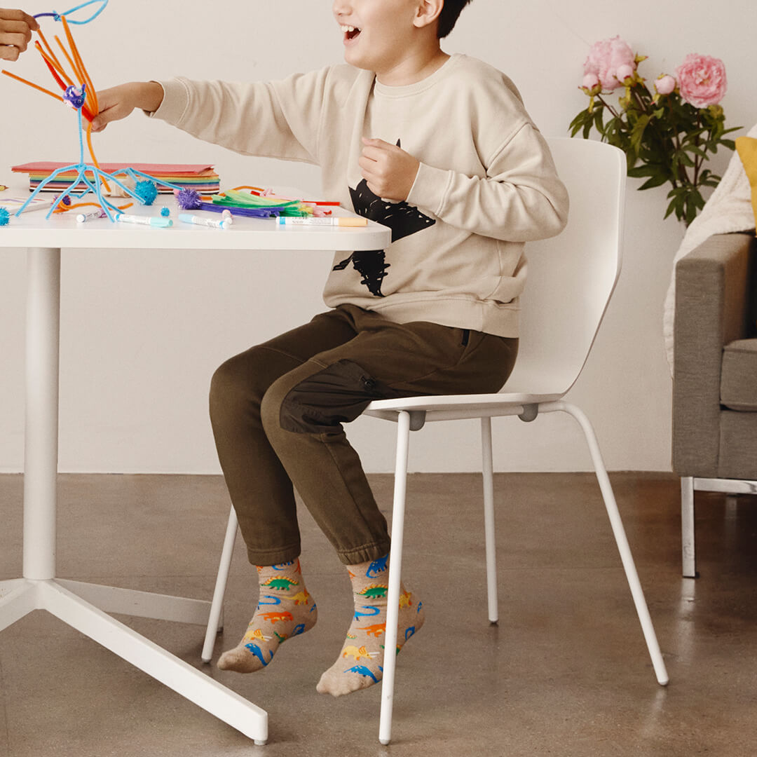 Child sitting at a table playing with colorful toys in a room with a couch and flowers.
