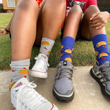 Two pairs of feet wearing colorful taco socks and sneakers on a grassy background