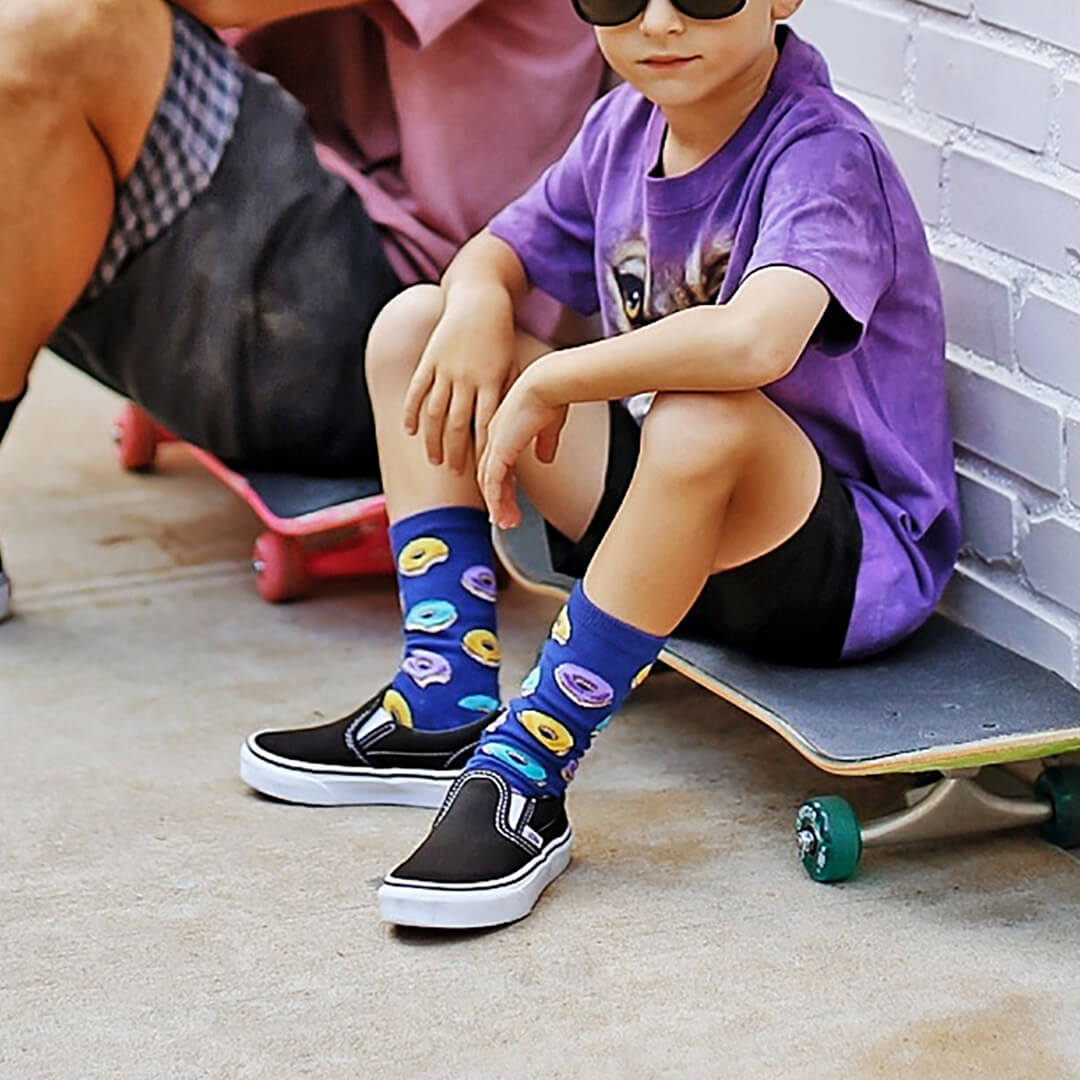 Child sitting on a skateboard wearing colorful socks with a brick wall background