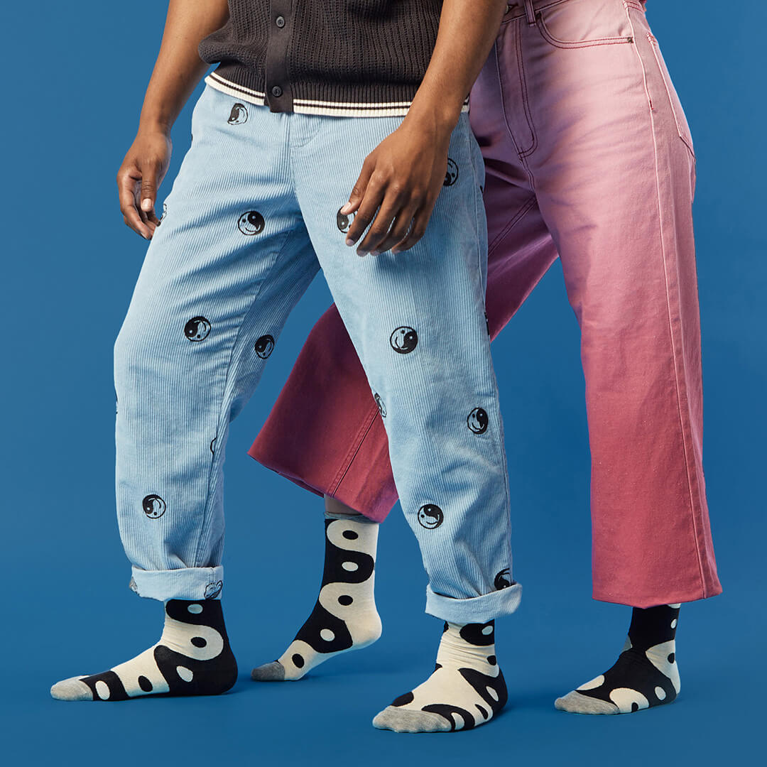 Two people wearing jeans with decorative patterns and black and white patterned yin yang socks on a blue background.