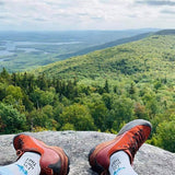 Red hiking boots on a rock with a scenic view of green hills and lakes. thumbnail