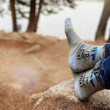 Person wearing socks with text and graphics, sitting on a rock outdoors.