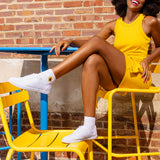Woman in yellow dress and white sneakers sitting on a yellow chair against a brick wall. thumbnail