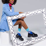 Woman in a blue outfit with matching socks and shoes sitting inside a decorative frame. thumbnail
