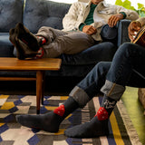 Two people sitting on a couch with one wearing socks featuring dice designs. thumbnail