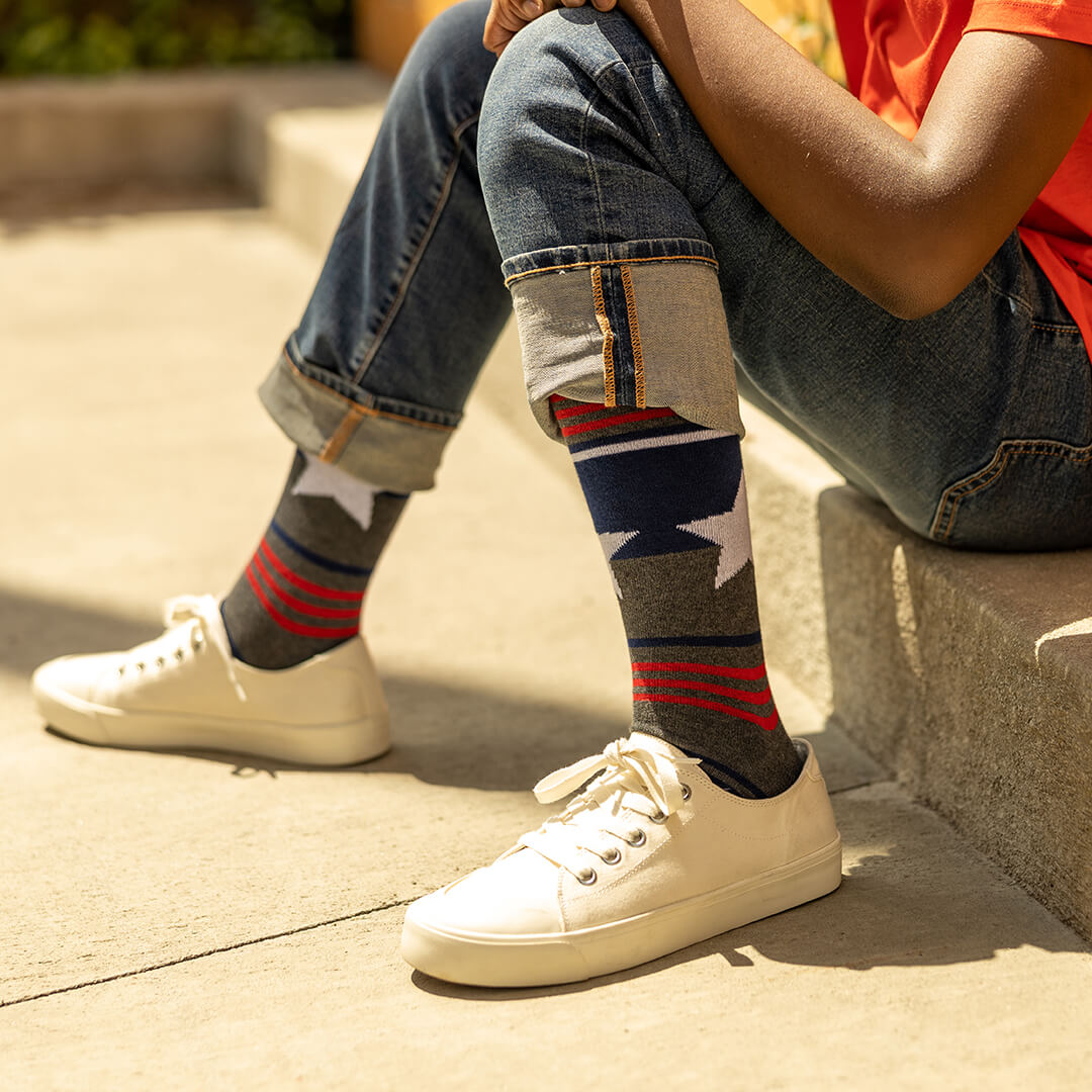 Person wearing white sneakers and colorful striped socks sitting on a concrete surface.