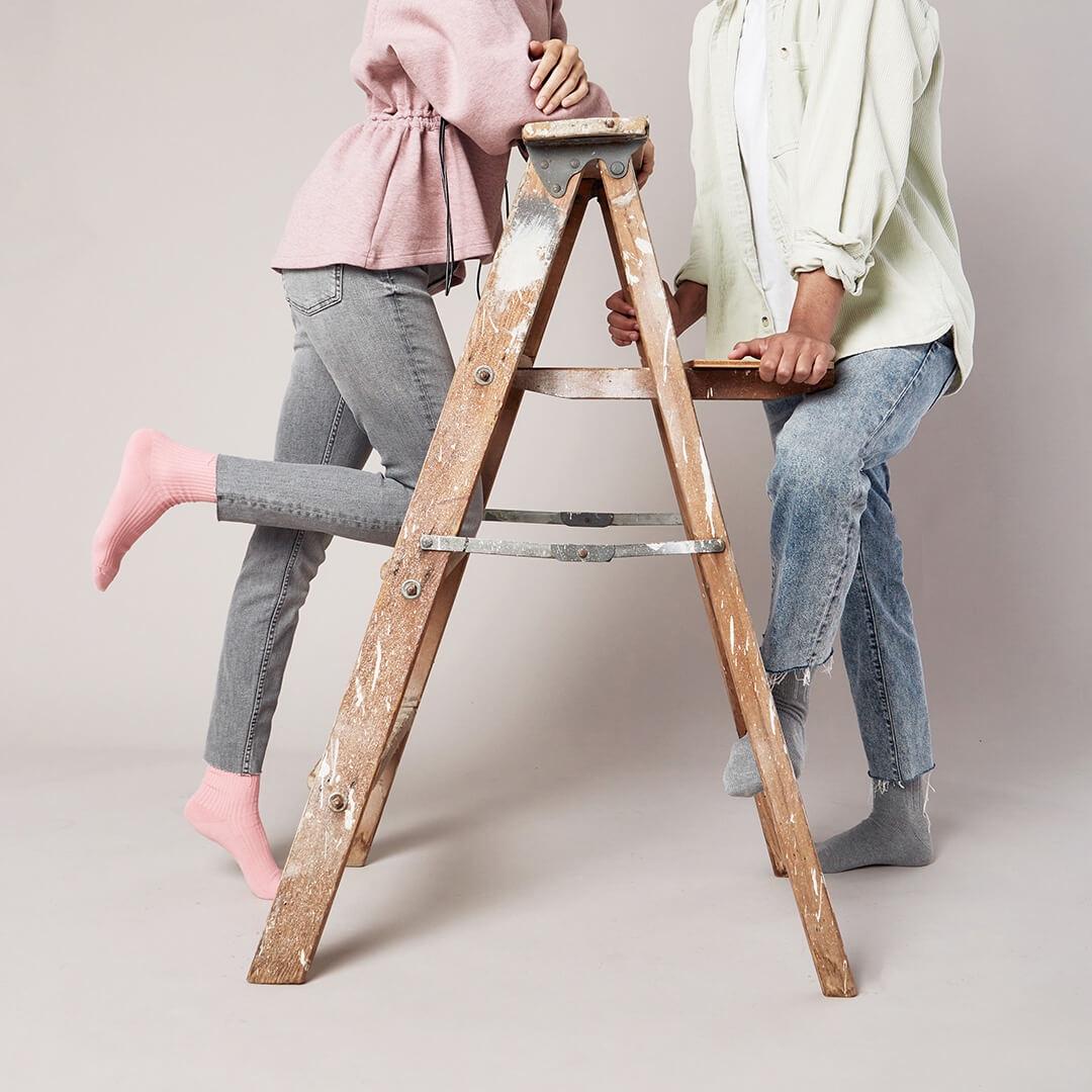 Two people using a wooden step ladder against a plain background