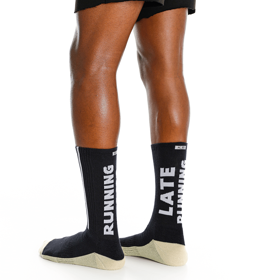 Black socks with 'RUNNING' and 'LATE RUNNING' text worn by a person on a white background