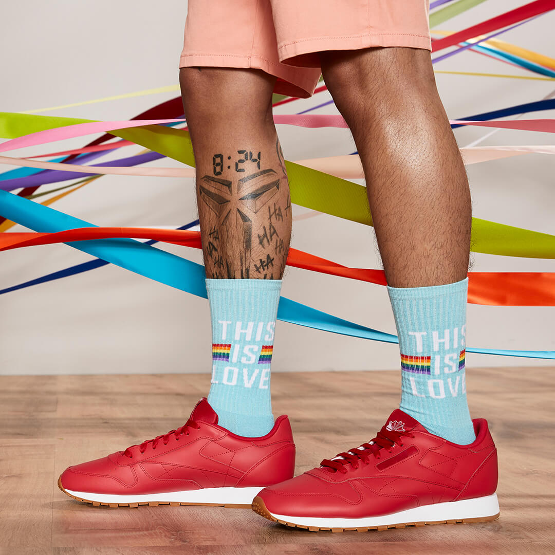 Person wearing light blue socks with 'This is Love' text and rainbow colors, red sneakers, on a colorful abstract background.