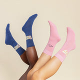 Two pairs of socks, one blue and one pink, on feet against a beige background. thumbnail