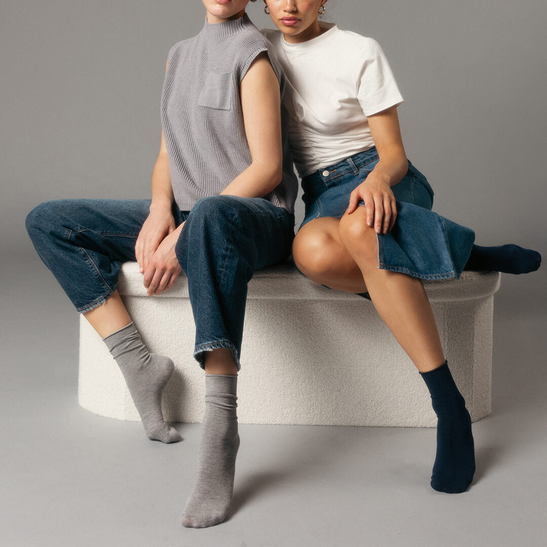 Two people sitting on a white stool wearing gray and black socks against a gray background