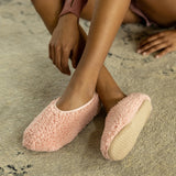 Person wearing pink fuzzy slippers on a carpeted floor