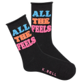 A pair of black fuzzy socks with the text 'All The Feels' in blue and pink colors, and the brand name 'K.Bell' at the end of the foot.