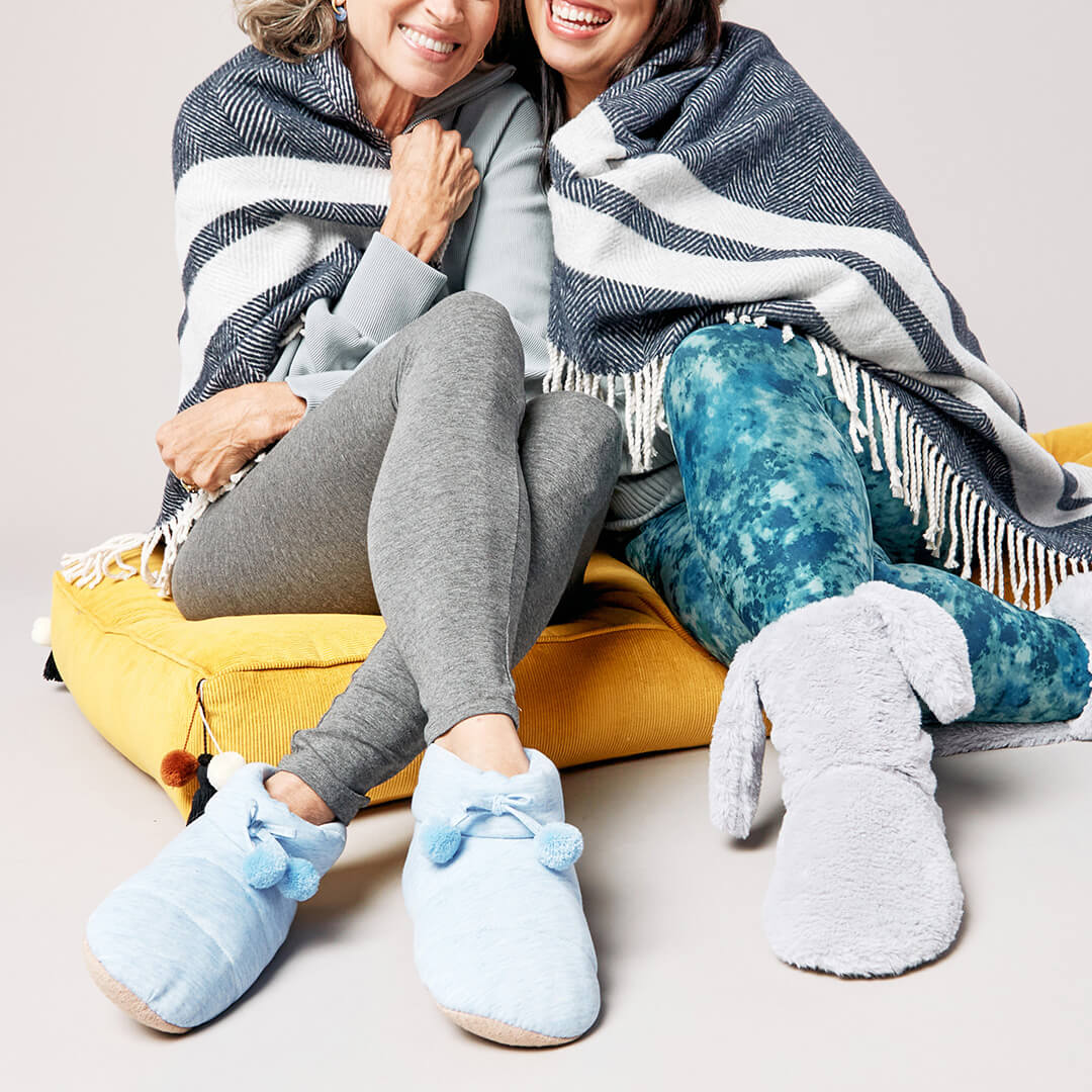 Two people sitting together wrapped in a blanket, wearing cozy slippers.