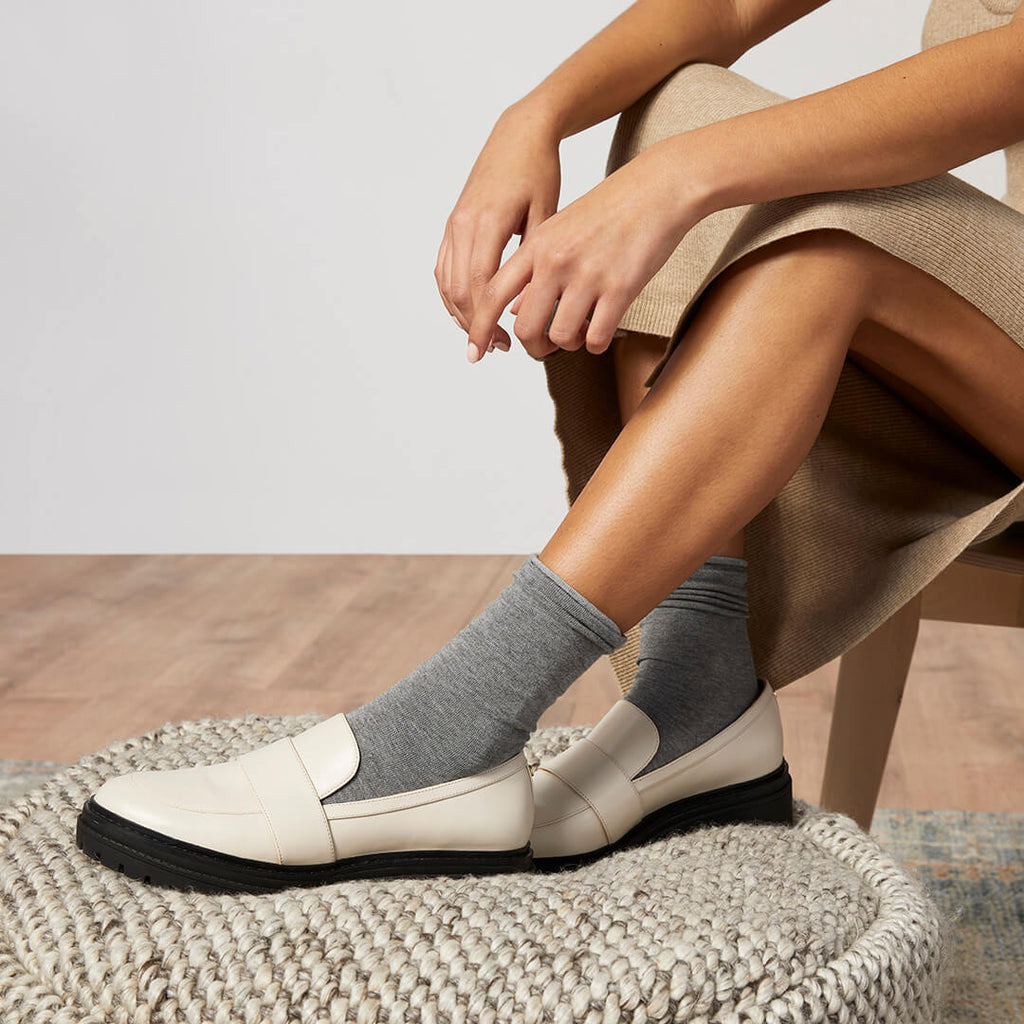 Person wearing white loafers and gray socks sitting on a textured surface.