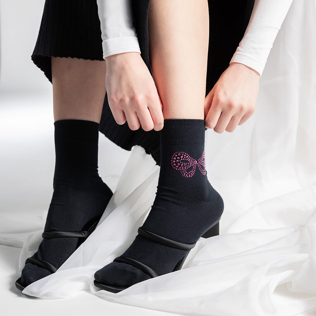Person wearing black socks with a Black socks with a rhinestone bow design and 'k.bell' branding on a white background