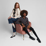 Two women sitting in fashionable outfits with k.bell socks on a pink chair against a plain background