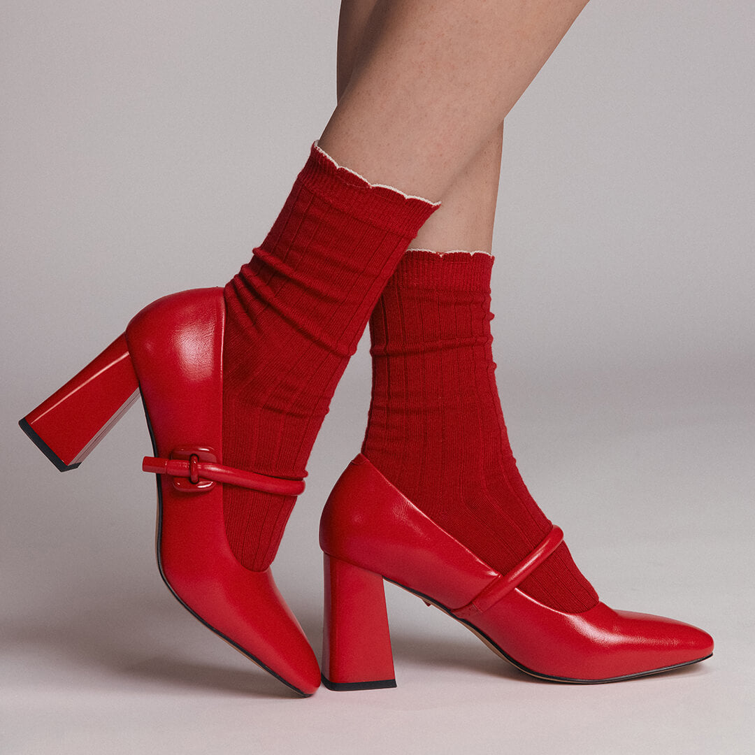 Red high-heeled shoes with matching socks on a neutral background