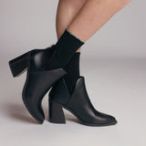 Black ankle boots worn with black socks on a neutral background