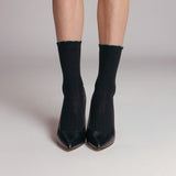 Black high-heeled shoes worn with black socks on a neutral background