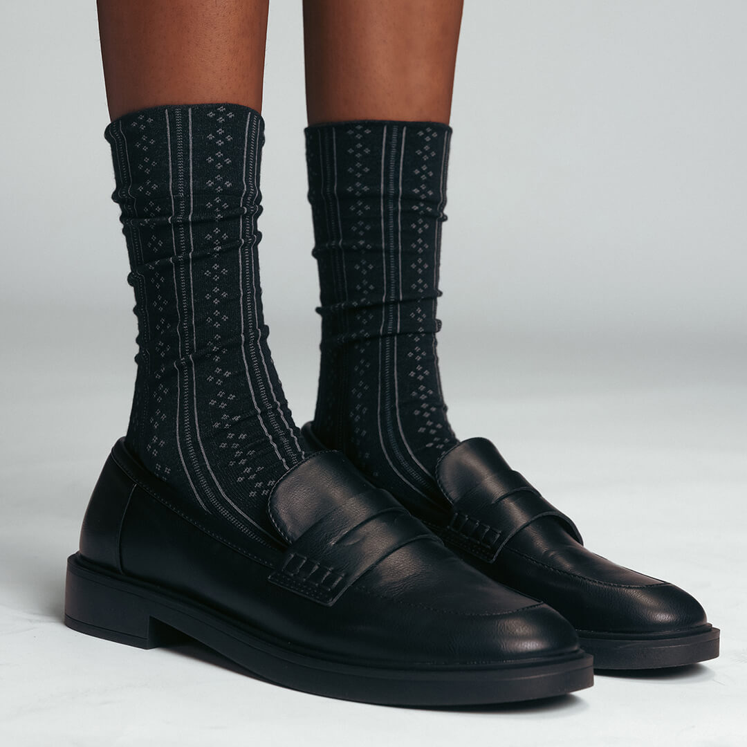 Black leather shoes with textured black  pointelle socks on a light gray background