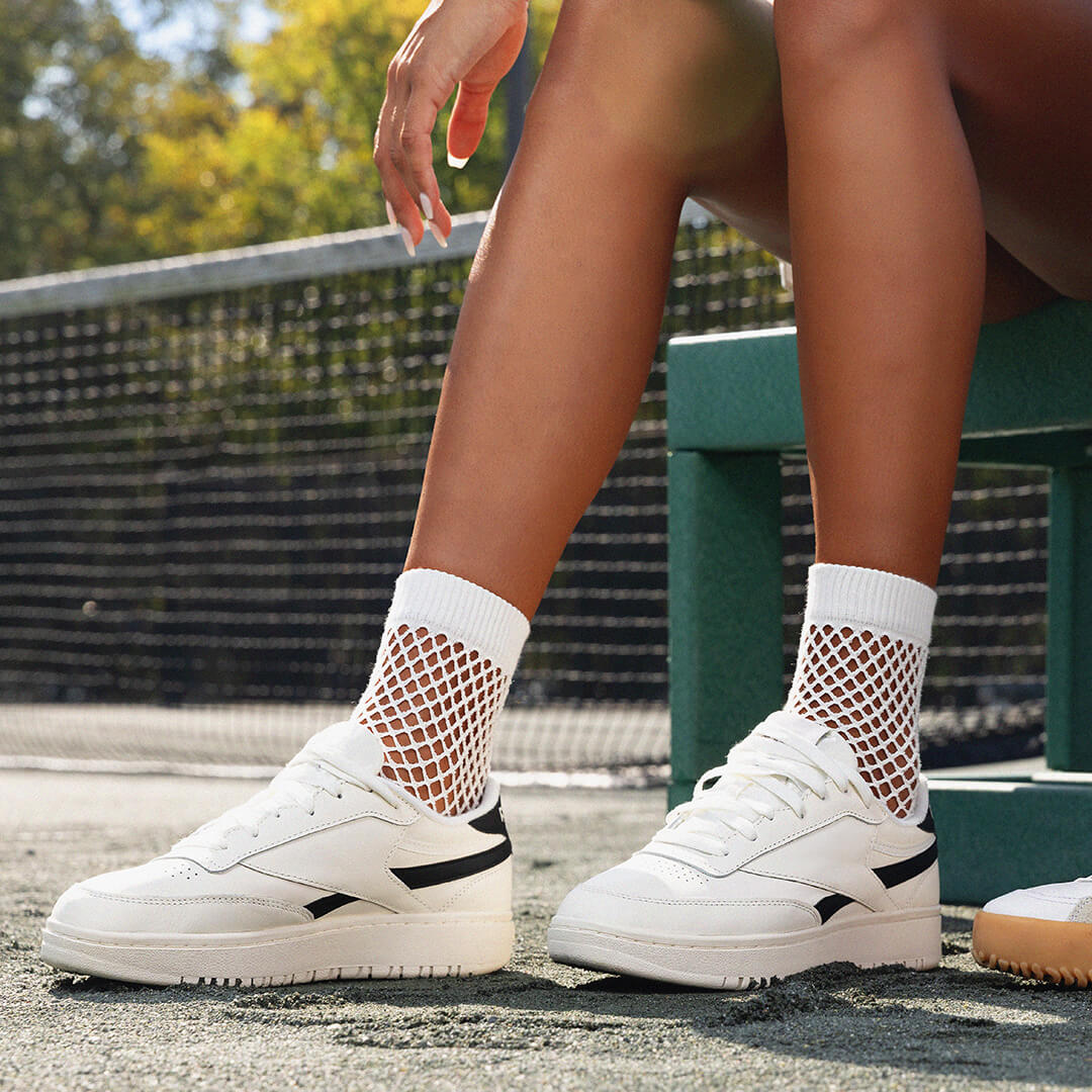 Person wearing white sneakers with black accents and crochet net crew socks outdoors.