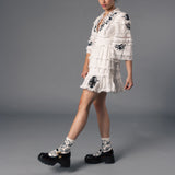 Woman wearing a white lace dress and socks with matching black floral accents on a gray background